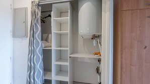 En walk-in-garderob med öppna hyllor, ett vitt element och en brandsläckare.