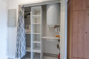A walk-in closet with open shelves, a white heater, and a fire extinguisher. - L'appartement Cala Nova (BORMES LES MIMOSAS)