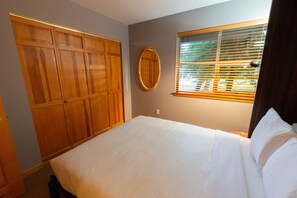 A bedroom with a bed, a wardrobe, a mirror, and a window with blinds. - Comfortable two-bedroom town home with room for the whole family (Whistler)