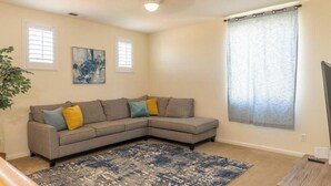 A living room with a gray sectional sofa, a blue patterned rug, and a painting on the wall.