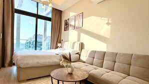 Ein modernes Hotelzimmer mit einem großen Bett, einer Couch, einem runden Couchtisch und Blick auf die Stadt durch das Fenster.