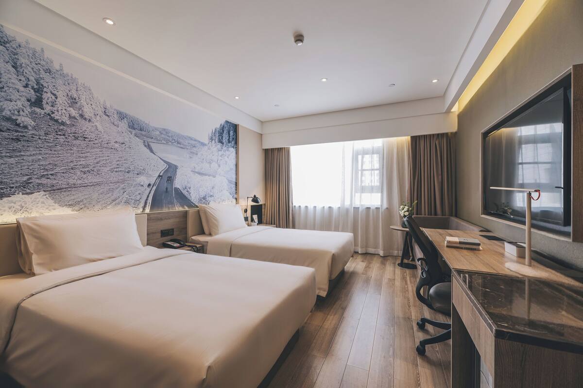Ein Hotelzimmer mit zwei Betten, einem Schreibtisch, einem Fernseher und einem großen Fenster.