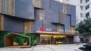 A modern hotel entrance with a glass facade, a red sign, and a landscaped area with seating. - Echarm PLUS Hotel Chongqing  (Chongqing)