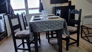 A dining area with a table set for four, surrounded by chairs, a television mounted on the wall, and a window with curtains. - T2 with breathtaking view of Lake Geneva (Lugrin)