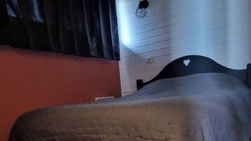 Un dormitorio con cama, piso de madera, pared roja y cortina negra.