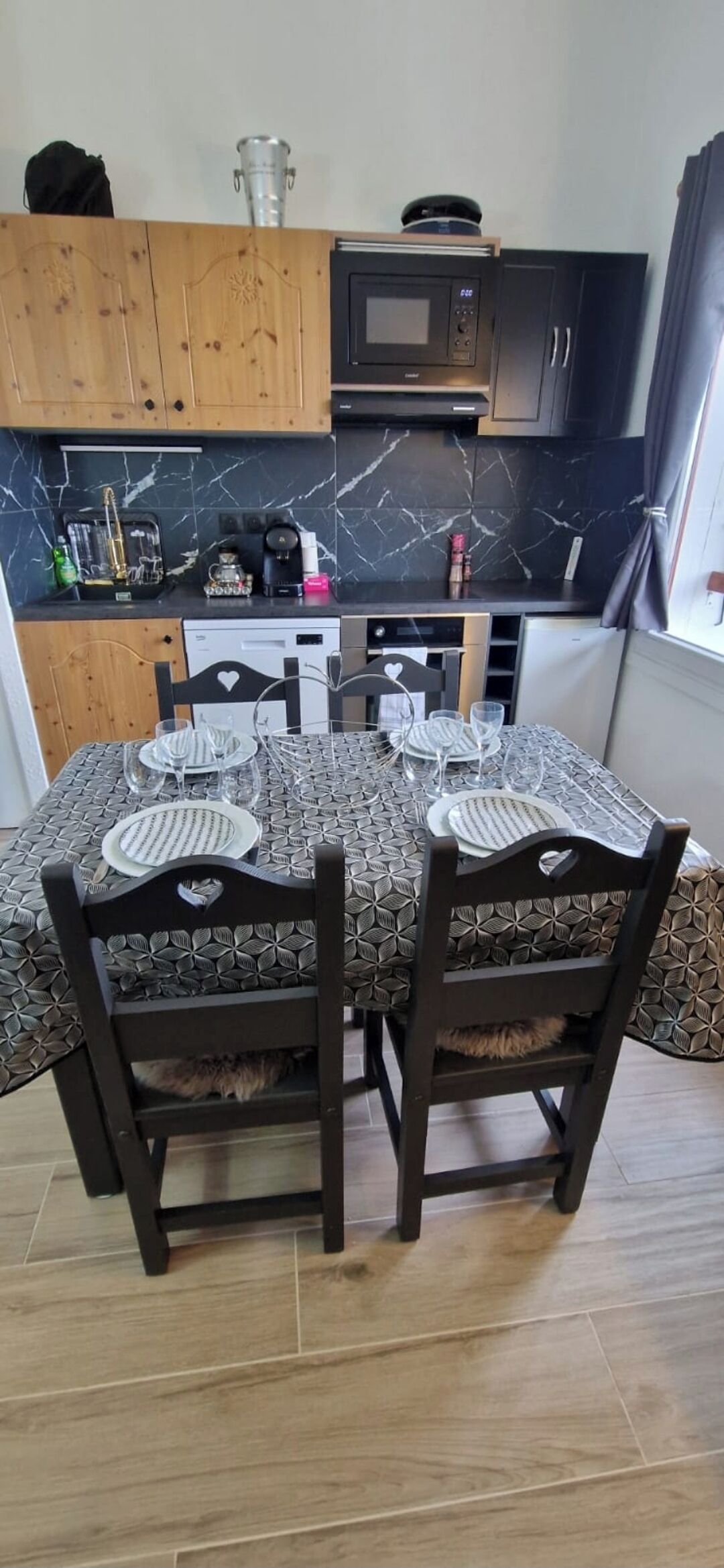 Een eethoek met een tafel voor vier personen, omringd door donkerhouten stoelen. In de achtergrond staan een magnetron en een koffiezetapparaat.