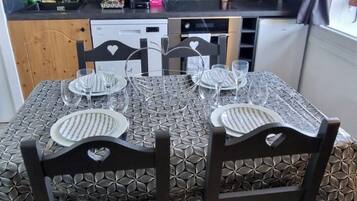 Een eethoek met een tafel voor vier personen, omringd door donkerhouten stoelen. In de achtergrond staan een magnetron en een koffiezetapparaat.