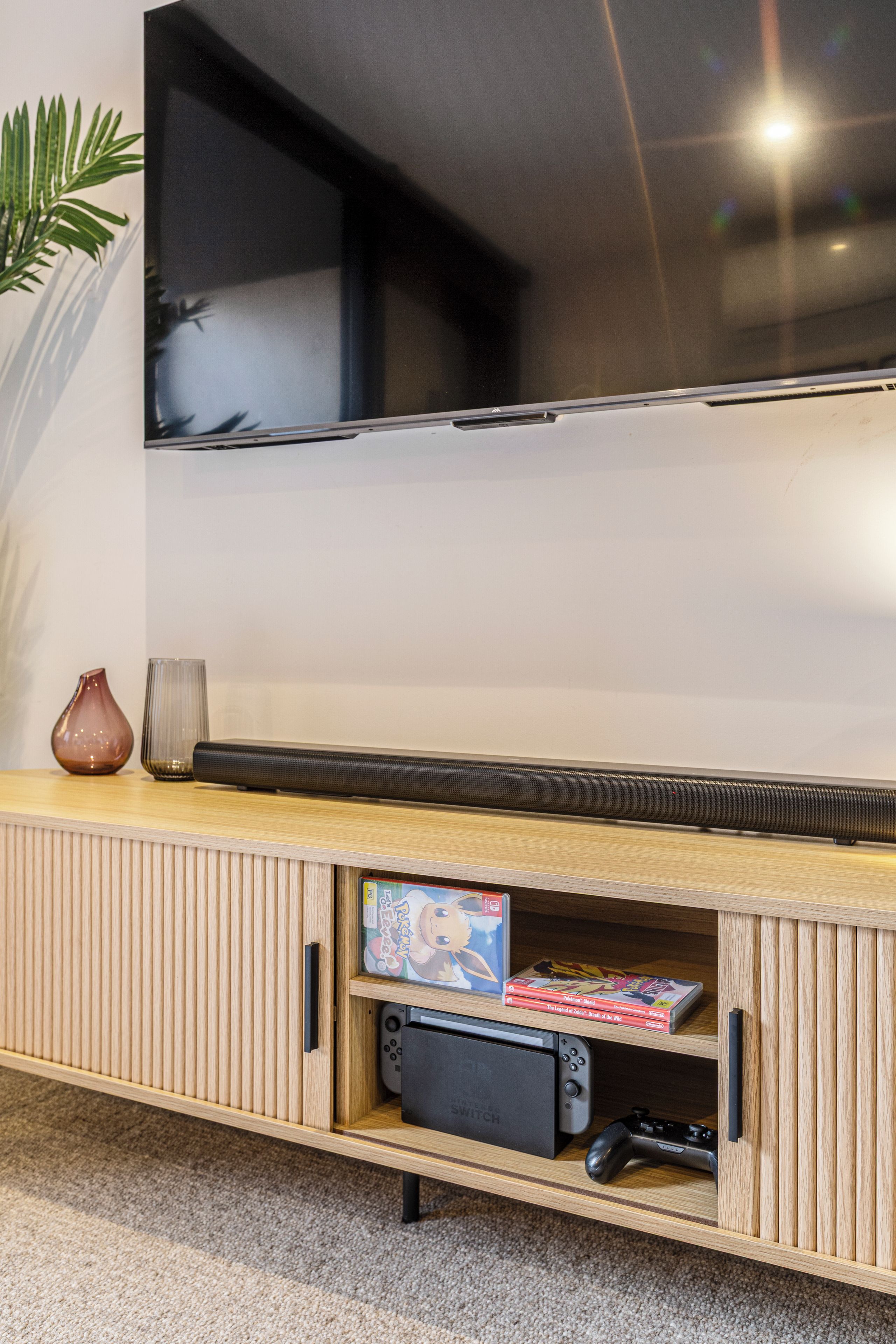 A flat-screen TV mounted on a wall above a wooden entertainment unit with a gaming console and video games.