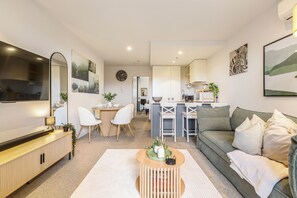 A modern living room with a sofa, a coffee table, and a dining area with chairs and a table. - Urban Oasis | Sleep 6 | Free Parking | Nintendo Switch (Collingwood)