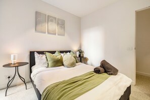 A neatly made bed with a green throw blanket, a bedside table with a lamp, and a wall-mounted artwork. - Urban Oasis | Sleep 6 | Free Parking | Nintendo Switch (Collingwood)