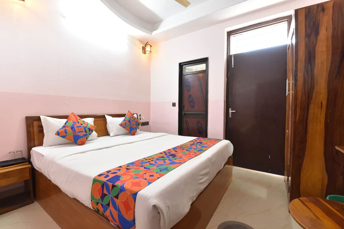 Quarto com cama, travesseiros, mesa de cabeceira, porta de madeira e luminária fixada na parede.