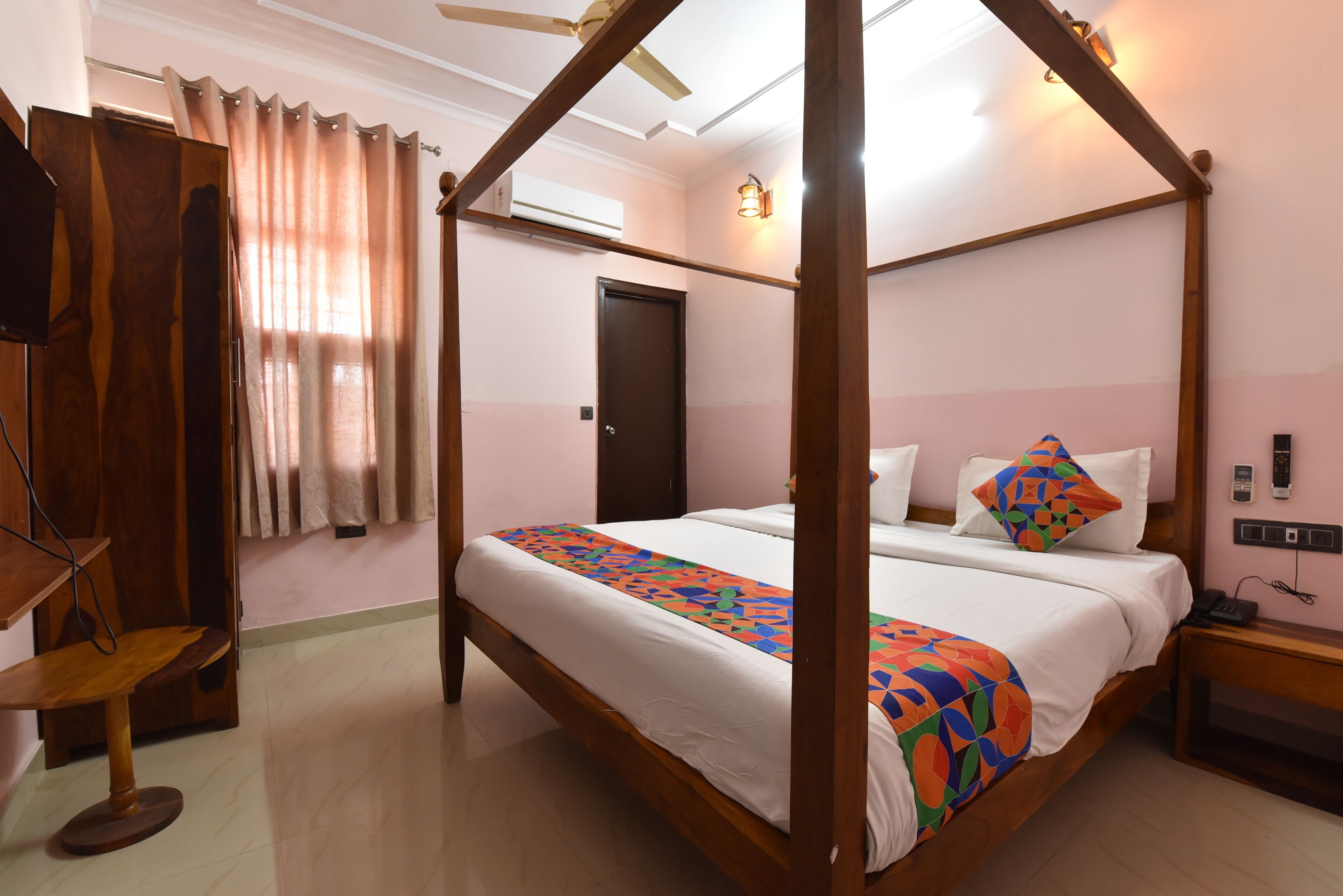 A four-poster bed with a colorful bedspread, a wooden nightstand, a desk with a chair, and a ceiling fan.