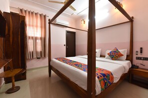 A four-poster bed with a colorful bedspread, a wooden nightstand, a desk with a chair, and a ceiling fan. - Hotel D7 (Jaipur)