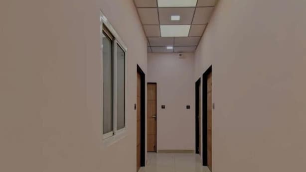 A corridor with a tiled floor, light pink walls, and doors on both sides. - Hotel D7 (Jaipur)
