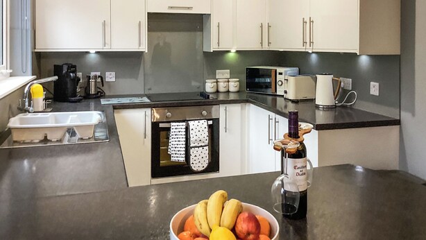 A modern kitchen with white cabinets, a built-in oven, a microwave, a coffee maker, and a bowl of fruit on the counter. - 2 bedroom accommodation in Tarves (Tarves)