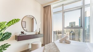 Moderni hotellihuone, jossa on suuri sänky, pyöreä peili, viherkasvi ja näkymä korkeisiin rakennuksiin.