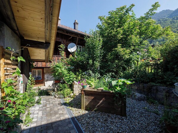 A rustic wooden building with a satellite dish, surrounded by lush greenery and a gravel path. - Beautiful apartment for 7 people with WIFI, TV, terrace, pets allowed and panoramic view (Brienzwiler)