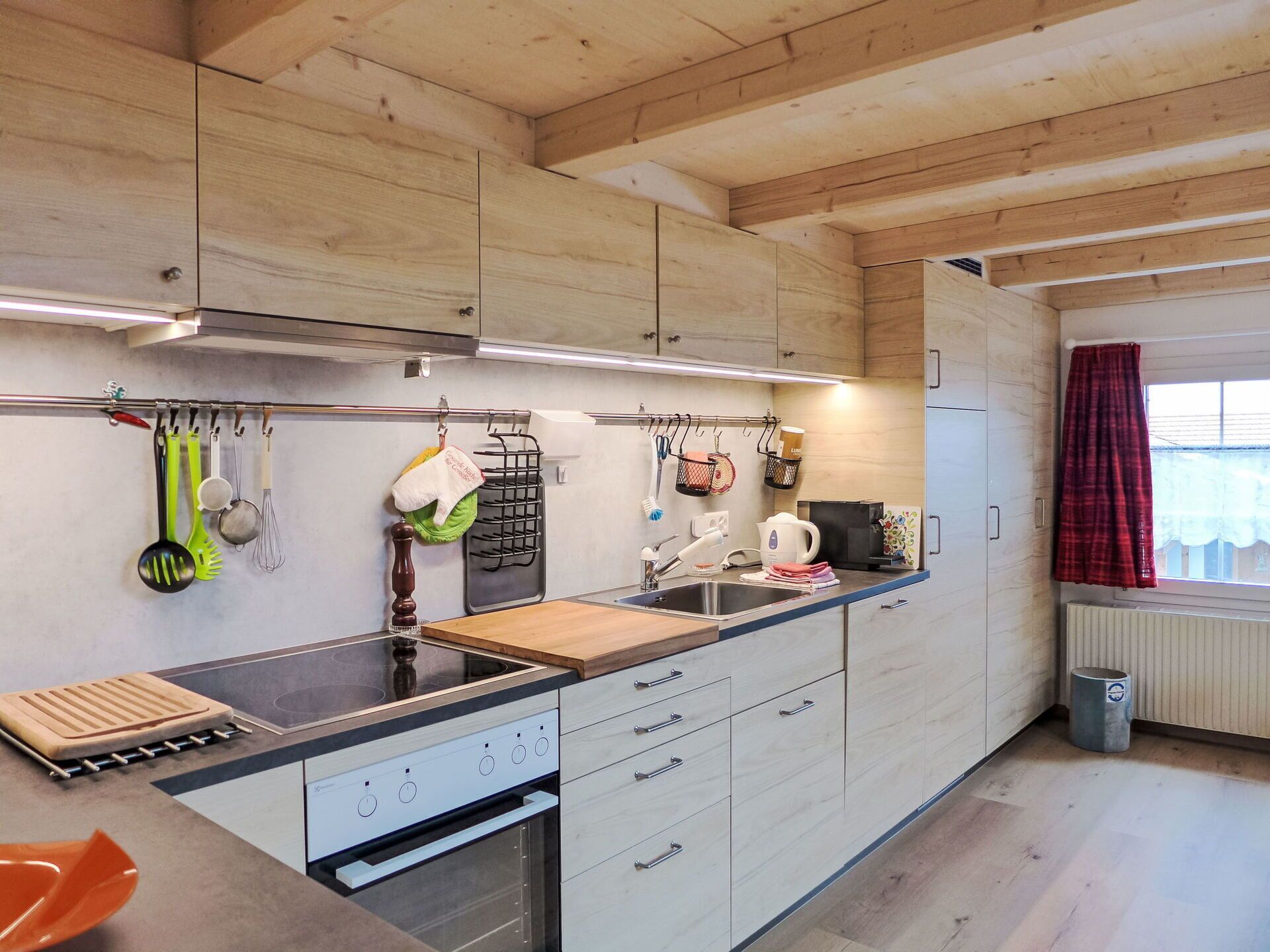 A modern kitchen with wooden cabinets, a built-in stove, and a countertop with various kitchen utensils.