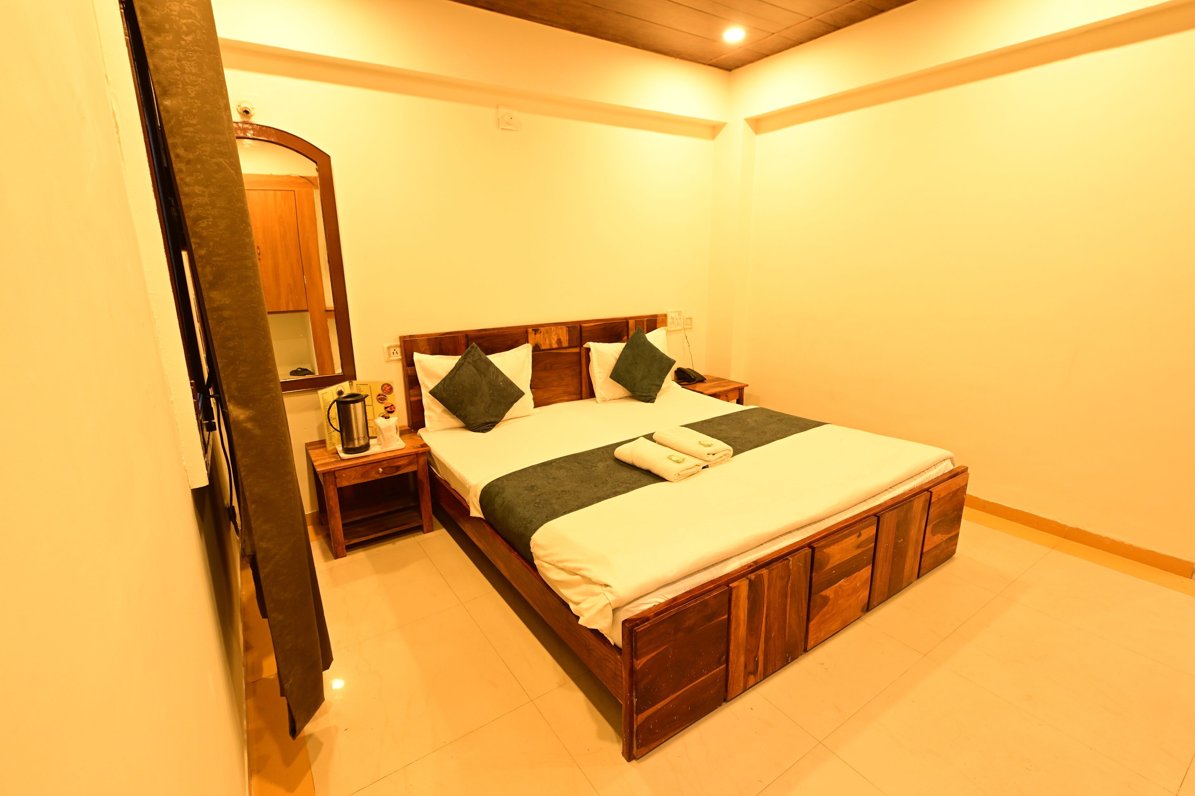 A neatly arranged bedroom with a wooden bed, a bedside table with a lamp, and a mirror on the wall.