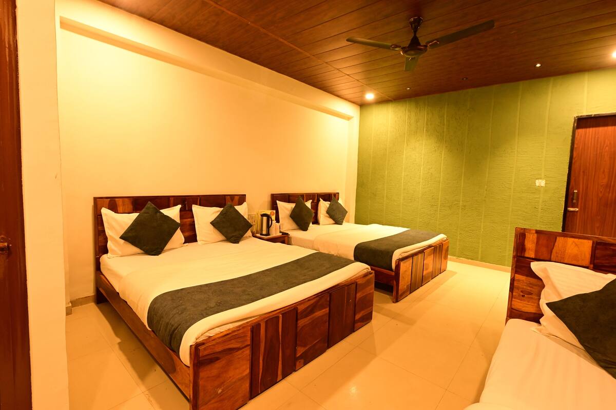 A hotel room with two wooden beds, a green accent wall, and a ceiling fan.