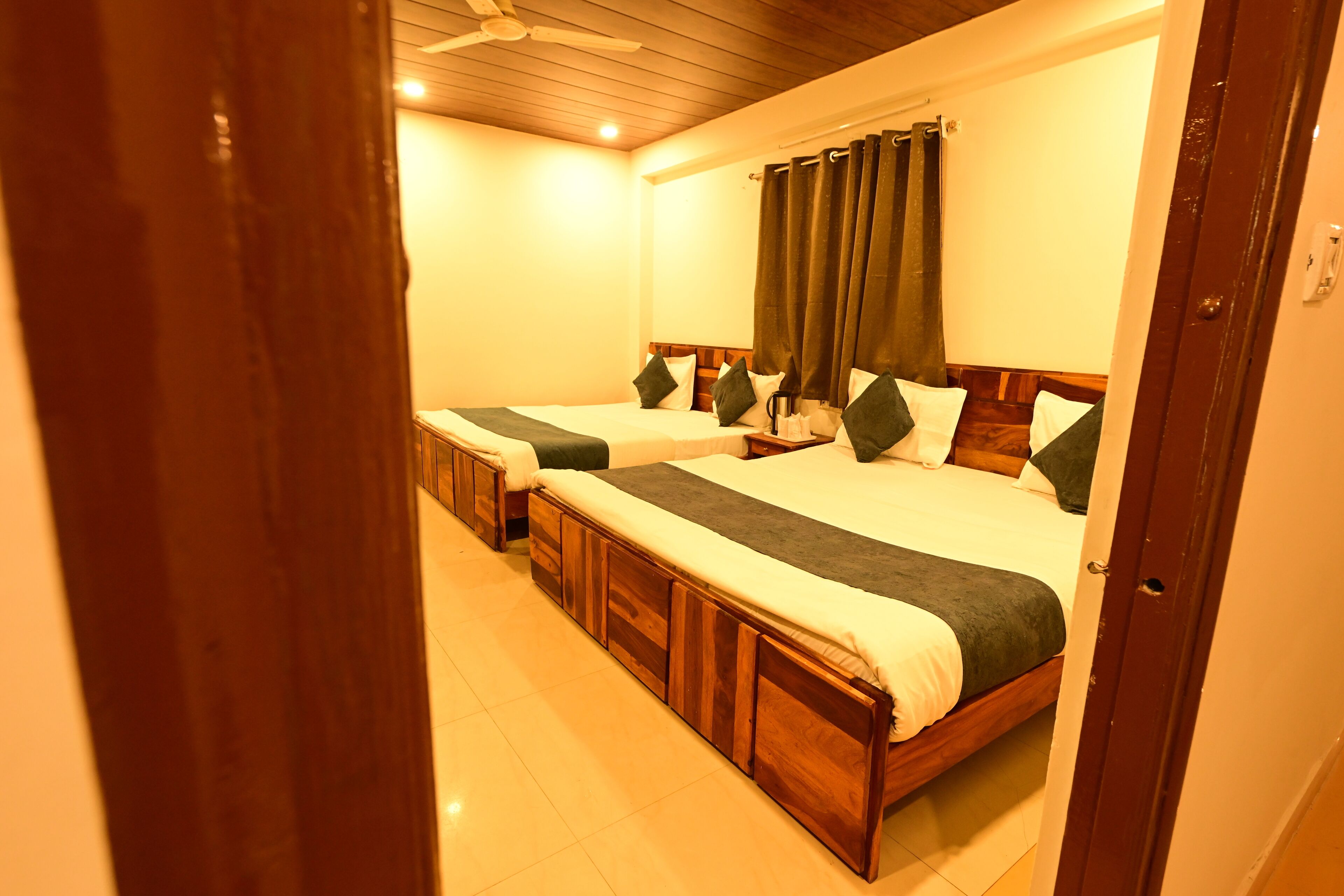 Une chambre d’hôtel avec deux lits simples, des têtes de lit en bois et une grande fenêtre avec des rideaux.