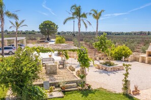 A patio area with outdoor seating, a pergola with vines, and a view of a vineyard in the background. - Trullo Tenuta Mary With Heated Pool (Carpignano Salentino)