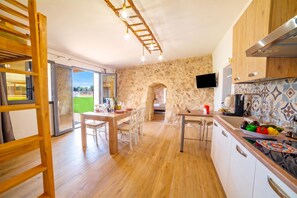 A modern kitchen with a stone wall, wooden cabinets, and a dining area with a table and chairs. - Trullo Tenuta Mary With Heated Pool (Carpignano Salentino)