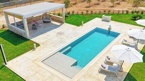 Ein rechteckiger Pool mit überdachter Sitzgelegenheit und Liegestühlen.