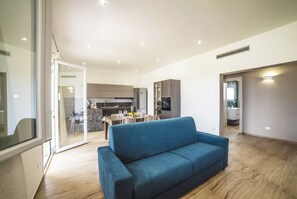 Un soggiorno moderno con un divano blu, una zona pranzo con tavolo e sedie, e una cucina sullo sfondo.