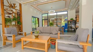 A modern living room with a sofa, two wooden chairs, a coffee table, and a plant shelf. - gangwanriji (Xuancheng)