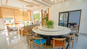 A modern dining area with a central round table surrounded by wooden chairs, a staircase leading to an upper level, and a view of the outdoors through large windows. - gangwanriji (Xuancheng)