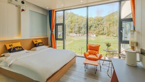 A modern bedroom with a large bed, a view of a green landscape, and a seating area with a table and chair. - gangwanriji (Xuancheng)