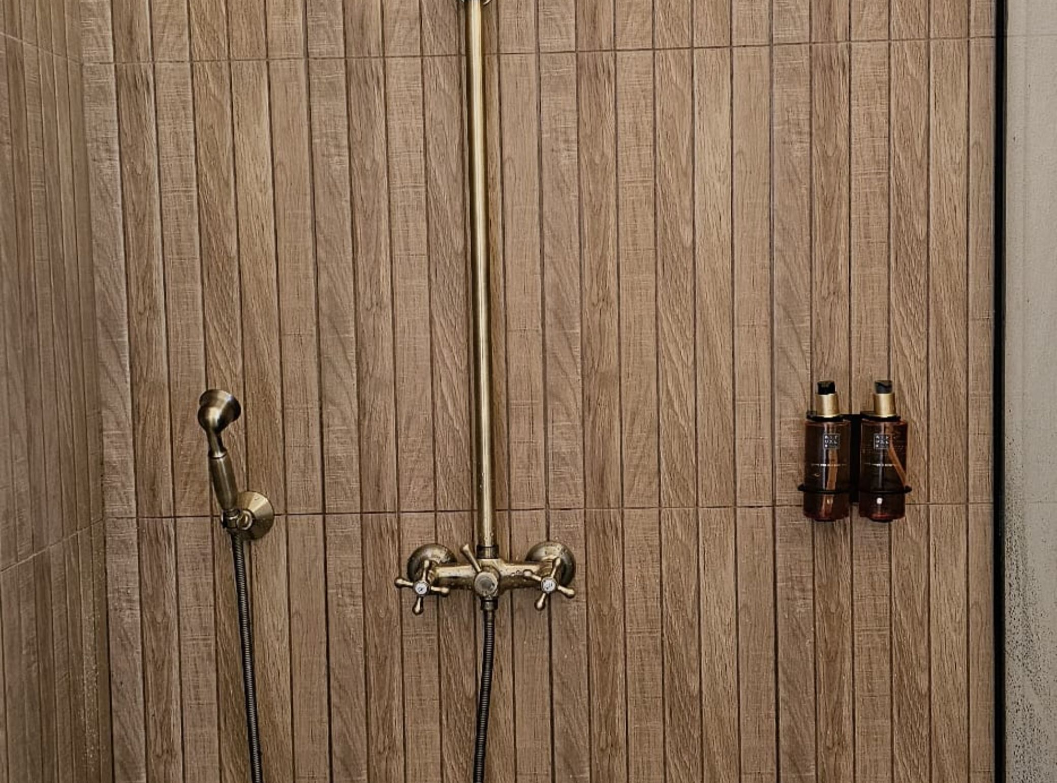 A wooden panel wall with a showerhead and two bottles of shampoo.