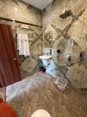 A bathroom with a marble wall, a sink, a mirror, a towel rack, and a toilet. - HR Palace (Varanasi)
