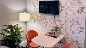 Un comedor con una mesa y sillas, una araña, un televisor en la pared y un pequeño árbol de Navidad.