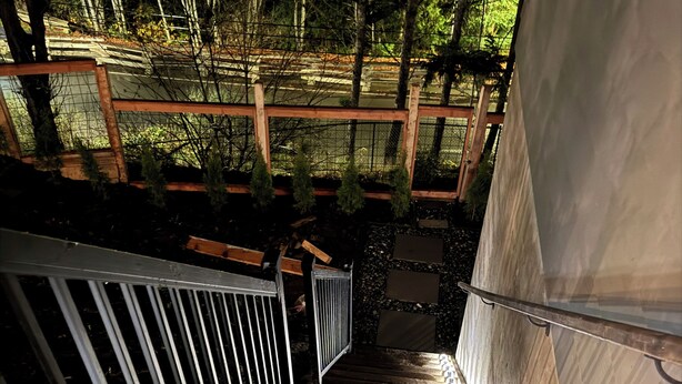Una escalera de madera con barandales de metal que conduce a un espacio al aire libre techado, con una terraza de madera y vistas a árboles.