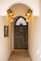 A hallway with a large, ornate door, two wall-mounted lights, and framed pictures on the wall.
