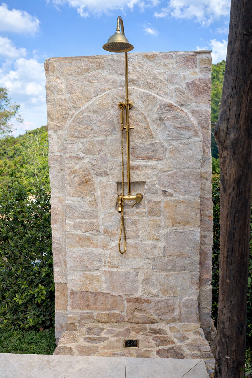 Pared de piedra con ducha y manguera dorada.