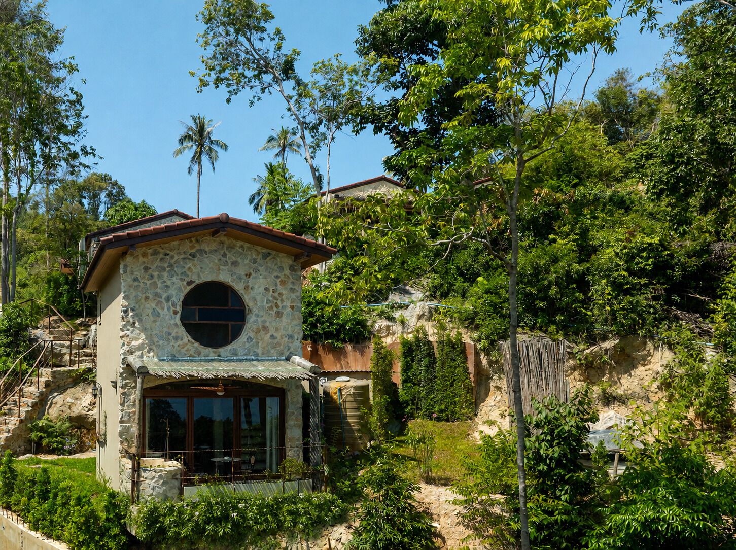 A stone building with a circular window, surrounded by lush greenery and a clear sky.