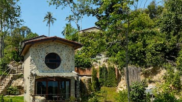 A stone building with a circular window, surrounded by lush greenery and a clear sky.