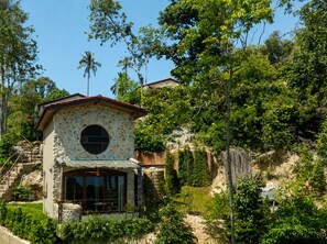 A stone building with a circular window, surrounded by lush greenery and a clear sky.