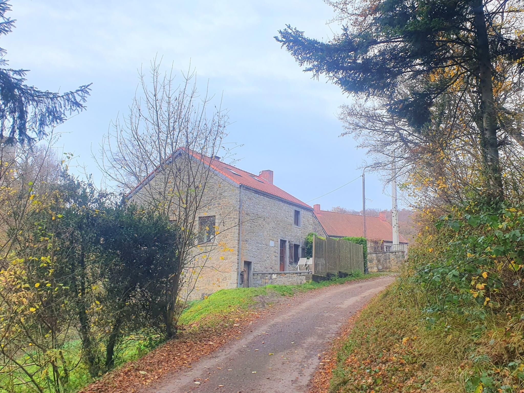 A stone house with a red roof, surrounded by trees and a dirt path.