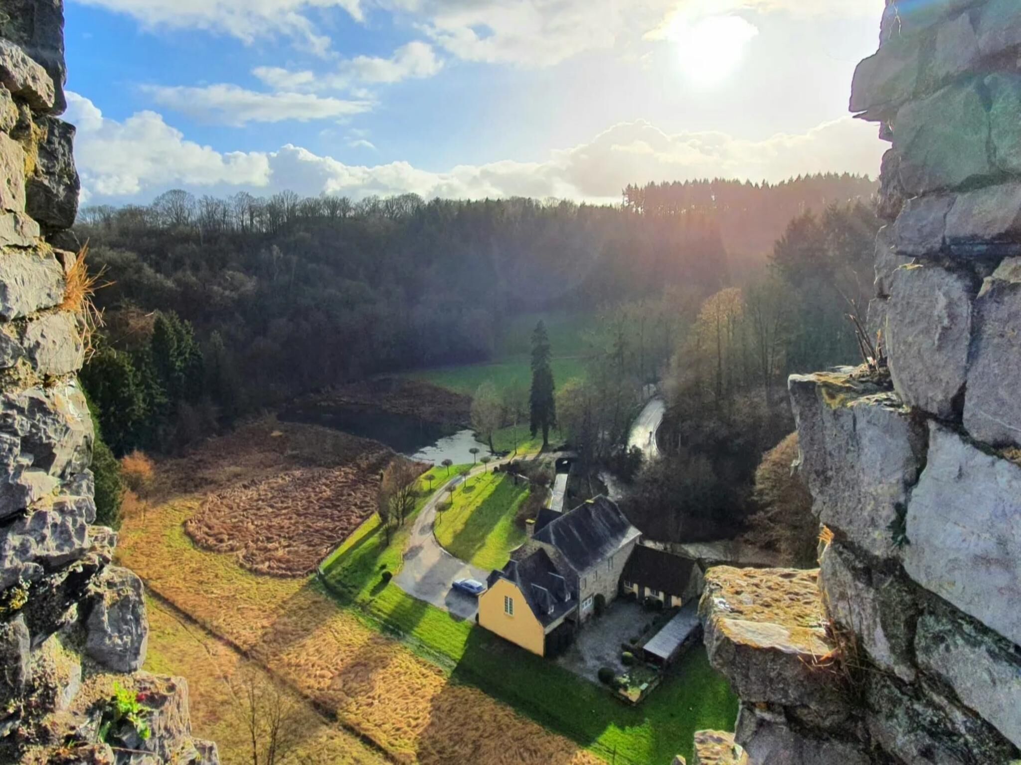 Eine ländliche Landschaft mit einer Steinmauer, einem kleinen Gebäude mit grüner Dachdeckung und einem Fluss.