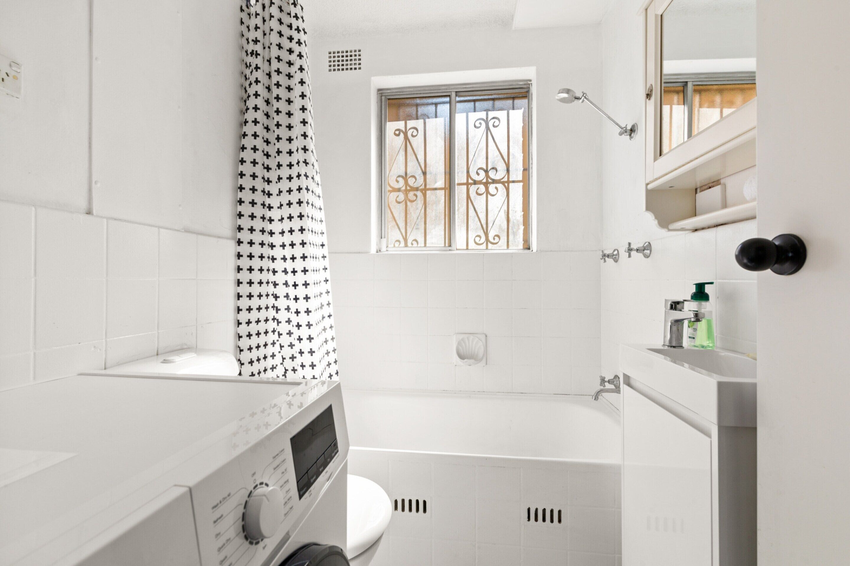 A modern bathroom with a white toilet, a bathtub, and a window with decorative bars.