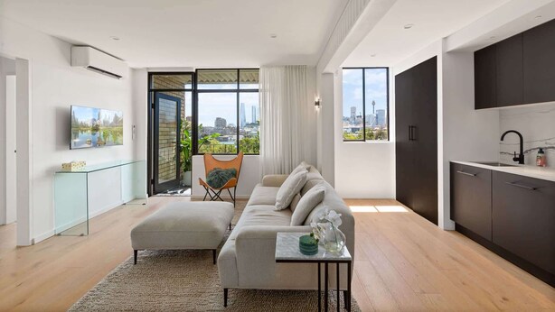 A modern living room with a sofa, ottoman, and a small side table with a vase of flowers. - Bright 2-Bed Apt with Spectacular Bridge Views (Glebe)