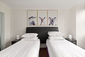 A hotel room with two beds, a dark headboard, white bedding, and three framed animal portraits on the wall. - Luxe CBD Apt | Hyde Park Views + Pool & Gym & Spa (Darlinghurst)