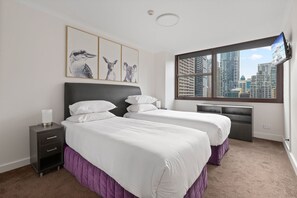 Habitación de hotel con dos camas, una mesita de noche, un televisor y vista a la ciudad.