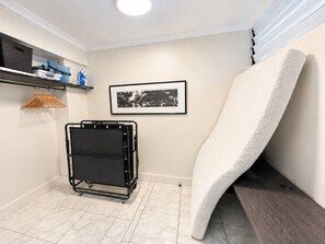Una habitación con un carrito metálico negro, una fotografía blanco y negro enmarcada en la pared y una toalla blanca apoyada contra la pared.