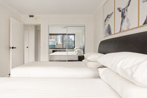 Habitación de hotel con cama, vista a la ciudad a través de una ventana y puerta que da a otra habitación.