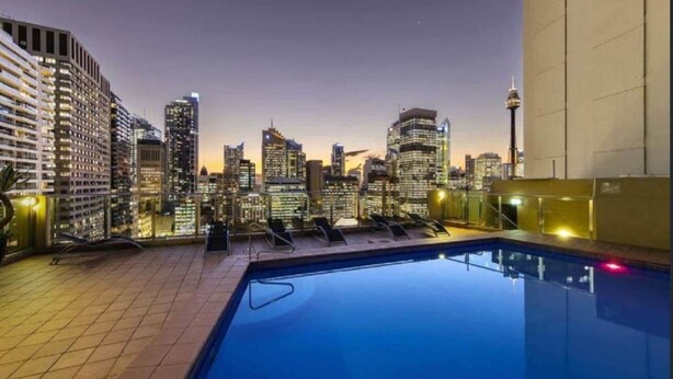 Une piscine sur le toit offrant une vue sur la ville, des chaises longues et une façade moderne.